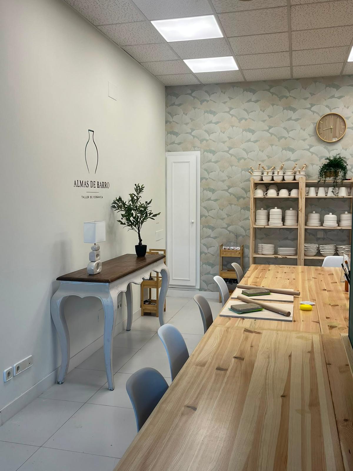Mesa comunal de madera y estanterías de piezas de bizcocho en el taller Almas de Barro
